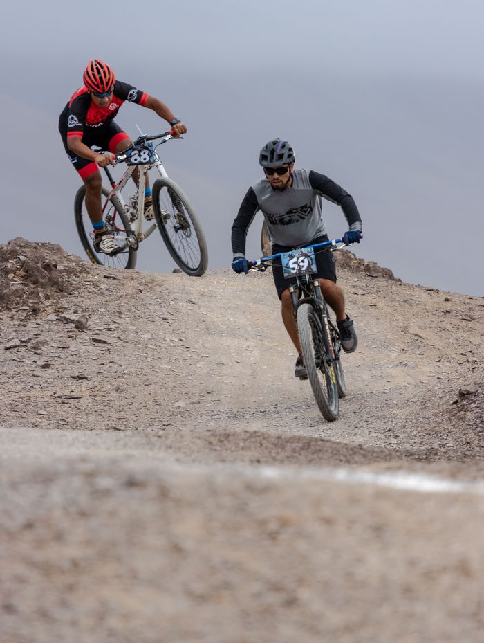 Two cyclists compete intensely on a rugged mountain path engaging in a thrilling race.