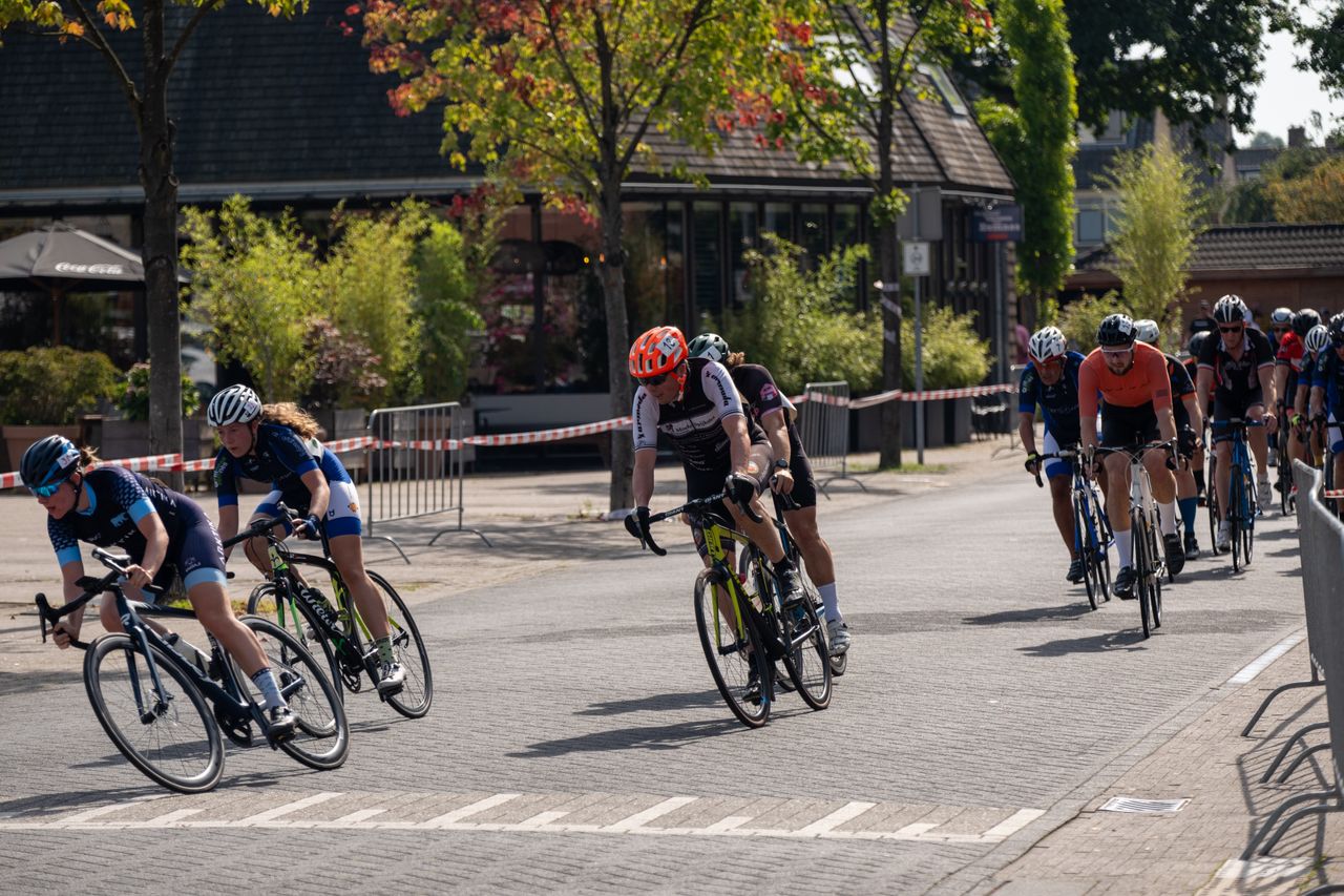 Group of competitive cyclists racing on urban streets during a sunny day event.