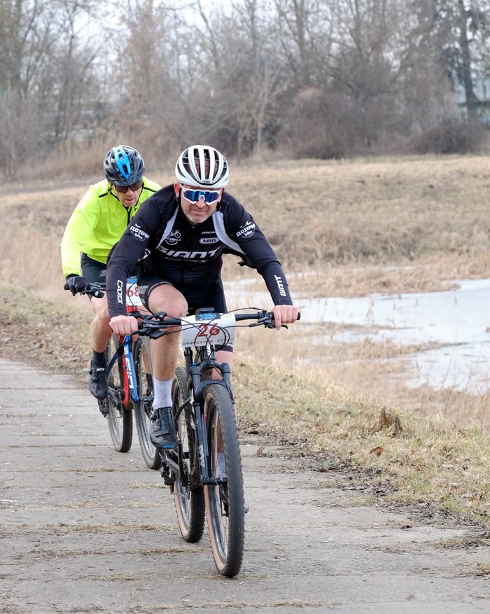 Two cyclists in sports gear competing on a rural path during a bike race in early spring.